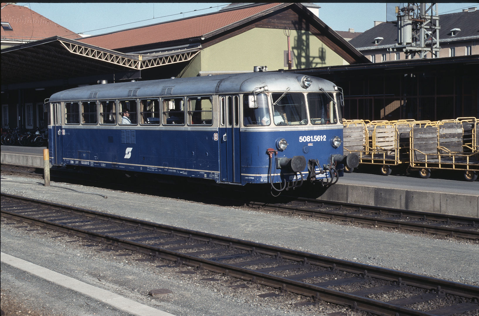 Blauer ÖBB-Triebwagen 50815612 steht auf Gleisen mit Güterwagen daneben